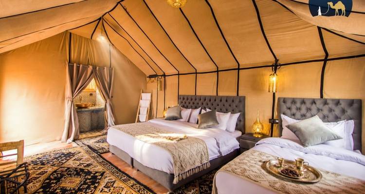 Intérieur luxueux de tente du désert avec deux grands lits, tapis à motifs, lanternes en laiton et éclairage d'ambiance chaleureux.