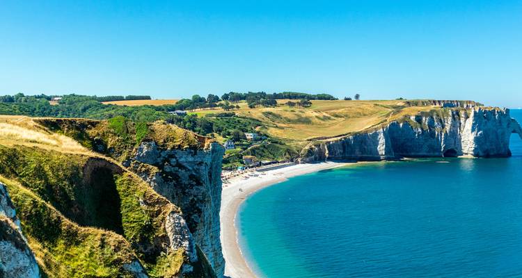 Espectaculares acantilados blancos de tiza y bahía turquesa de Étretat se curvan bajo un cielo azul claro de Normandía.