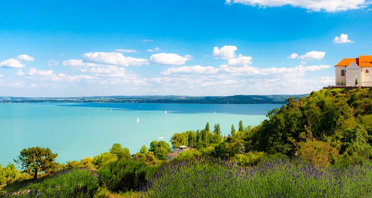 Une colline parsemée de lavande descend vers les eaux bleu pâle du lac Balaton avec des voiliers et l'abbaye de Tihany visibles.