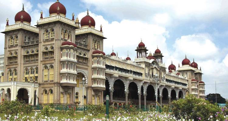 Majestic Mysore Palace with red domes and intricate arches under partly cloudy sky.