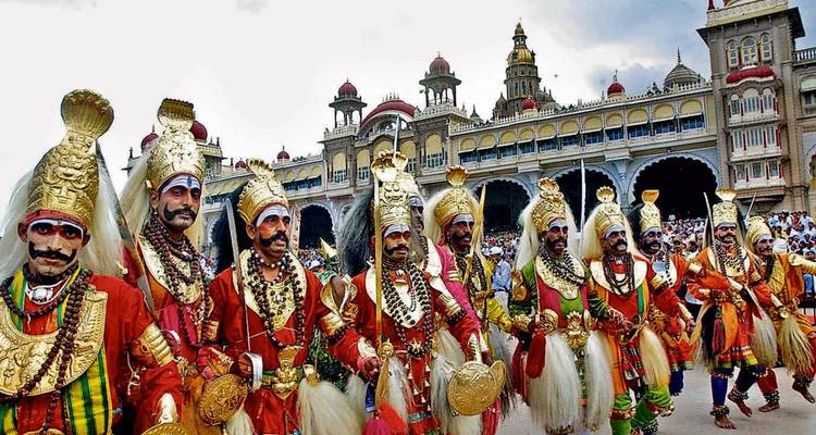 Vibrant costumed dancers parade outside Mysore Palace during festive celebration.