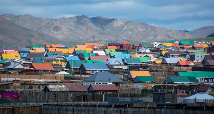 Bunte Dächer einer mongolischen Stadt breiten sich unter schroffen braunen Bergen aus