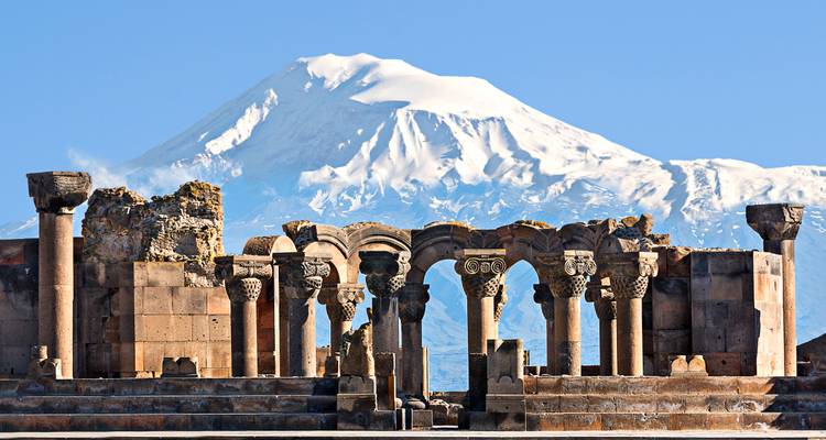 Antike Ruinen mit hohen Torbögen, eingerahmt vom schneebedeckten Berg Ararat unter klarem Himmel.