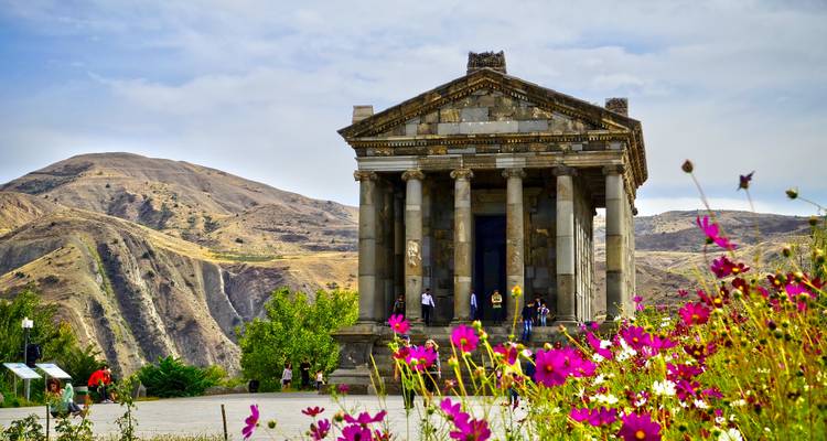 Garni-Tempel eingerahmt von bunten Wildblumen mit sanften Hügeln dahinter.