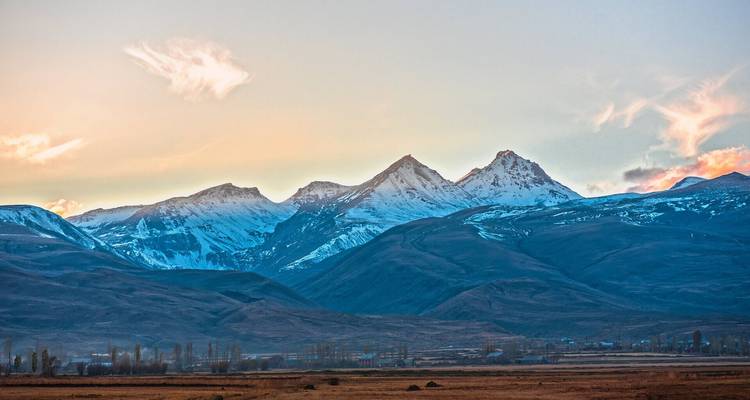 Schneebedeckte Berggipfel, die unter pastellfarbenem Abendlicht über einem weiten Tal leuchten