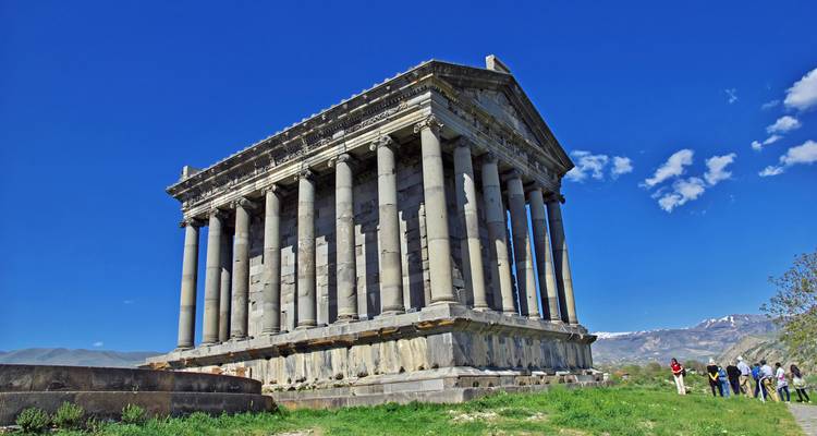 Klassischer griechisch-römischer Garni-Tempel mit Touristen, die in der Nähe unter einem strahlend blauen Himmel stehen.