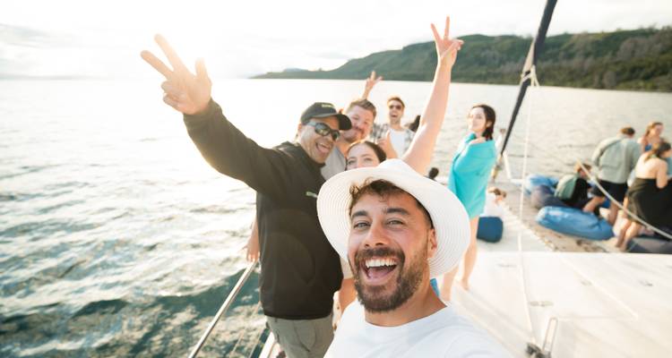 Selfie énergique de voyageurs faisant le signe de la paix sur un voilier au-dessus d'une eau scintillante.