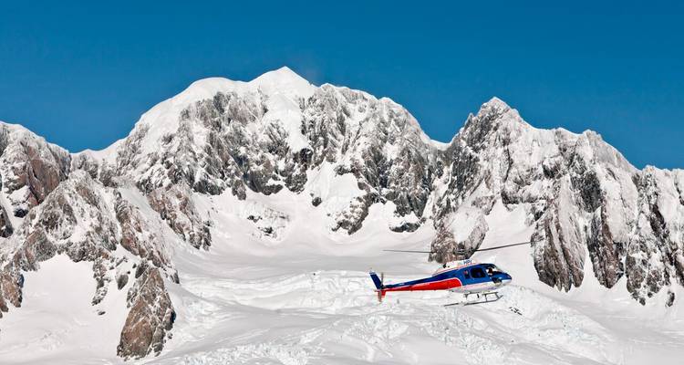 Un hélicoptère coloré s'est posé sur un vaste glacier enneigé sous des pics escarpés dans un ciel bleu profond.