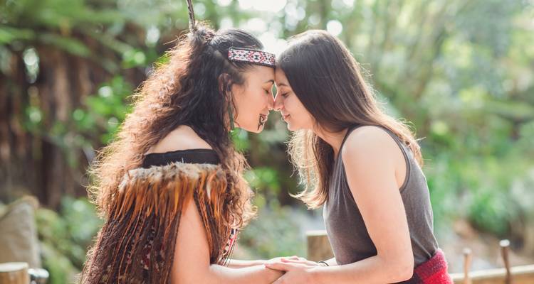 Gros plan de deux femmes partageant un salut traditionnel maori hongi au milieu de la verdure forestière.