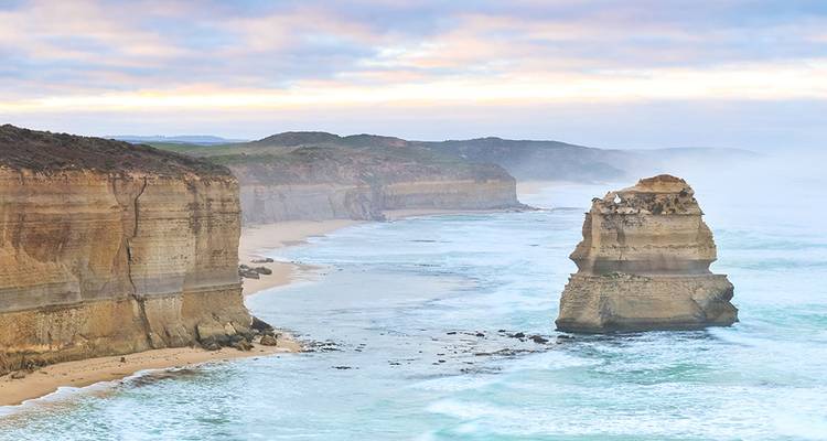 Les spectaculaires piliers calcaires des Douze Apôtres s'élèvent des vagues turquoise le long d'une côte brumeuse de la Great Ocean Road à l'aube.