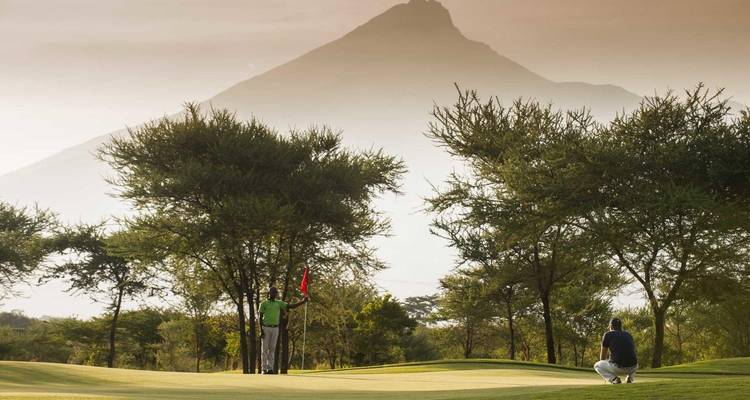 Golfers on a green with majestic Mount Meru silhouetted in the background