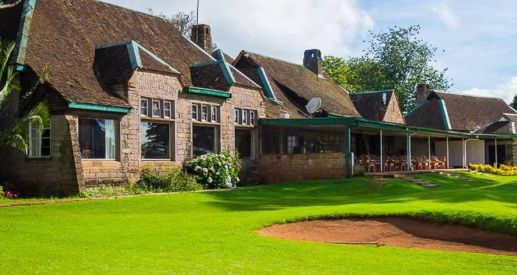 Stone clubhouse with green roofs overlooking a putting green and sand bunker
