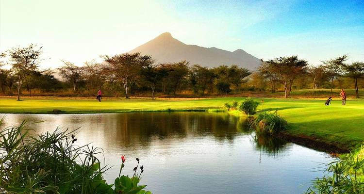 Golfers walk near a reflective pond with Mount Meru rising dramatically behind
