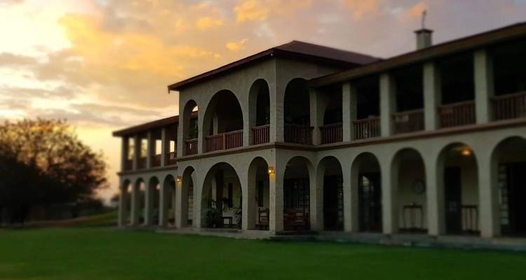 Colonial-style lodge with arched verandas silhouetted at sunset over a lawn