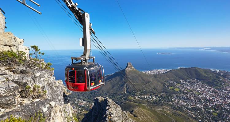 Red cable car ascending dramatic cliffs with panoramic ocean backdrop