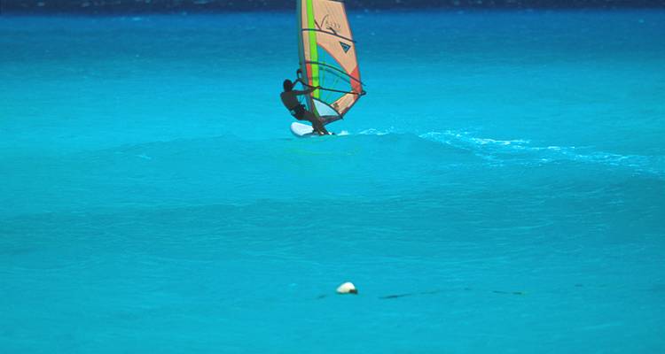 Windsurfista surcando las vibrantes aguas azules del Caribe bajo cielos despejados