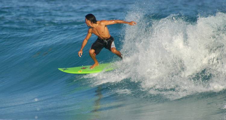 Surfista montando una ola rompiente en una tabla verde brillante en el mar azul claro