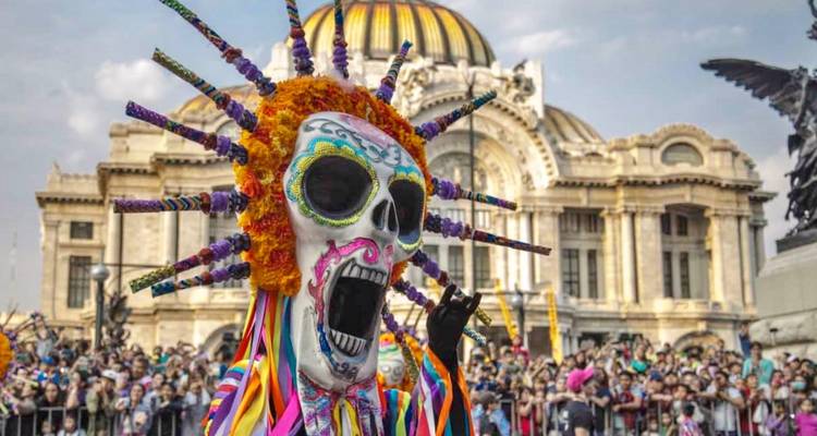 Vibrant skull costume during Day of the Dead parade with Palacio de Bellas Artes in the background.