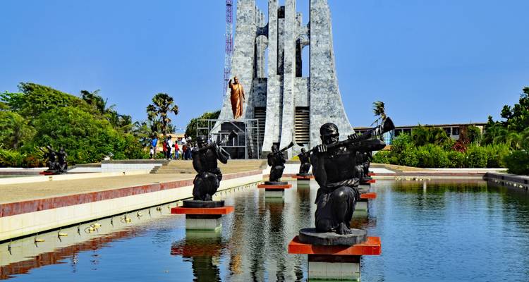 Kwame Nkrumah Mausoleum spiegelt sich in einem ruhigen Teich mit sitzenden Bronzestatuen und Besuchern in Accra wider.