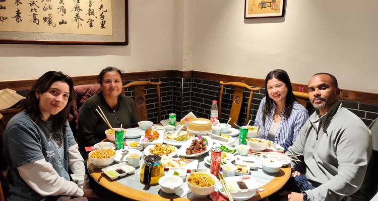 Cuatro viajeros comparten una mesa redonda llena de platos tradicionales chinos dentro de un restaurante acogedor.
