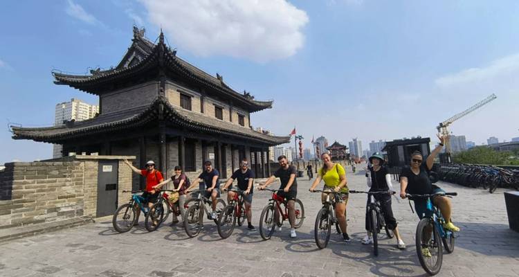 Los ciclistas se alinean con bicicletas sobre la antigua muralla de Xi'an junto a una torre de vigilancia histórica bajo un cielo brillante.