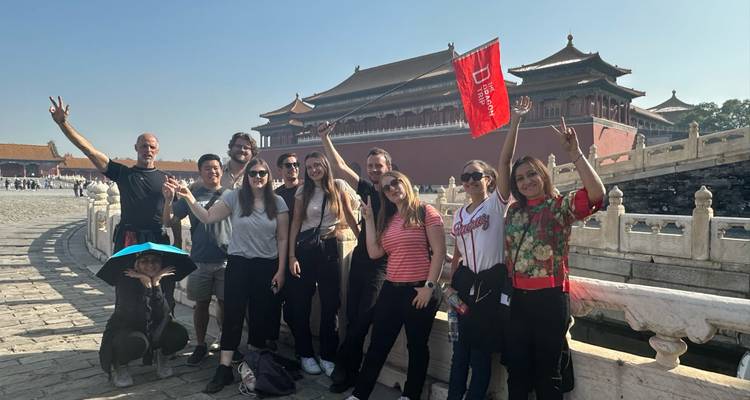Grupo de turistas hace gestos de paz dentro del patio de la Ciudad Prohibida con los salones del palacio al fondo.