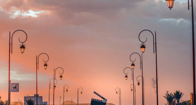 Lampadaires décoratifs se découpant en silhouette contre un ciel de coucher de soleil pastel avec une ville désertique au loin.