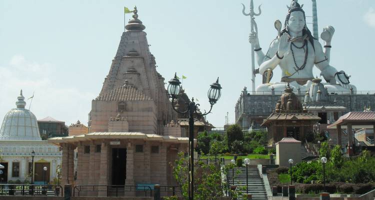 Große Shiva-Statue überragt Tempelkomplex mit verzierten Kuppeln and Gehwegen.