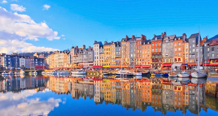 Waterfront vibrant de Honfleur avec des maisons historiques colorées reflétées dans les eaux calmes du port.