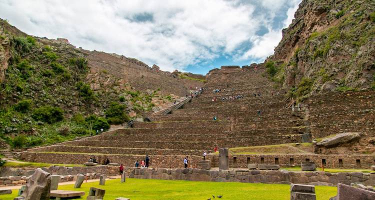 Vue large des ruines incas en terrasses à Ollantaytambo avec des visiteurs gravissant les marches de pierre.