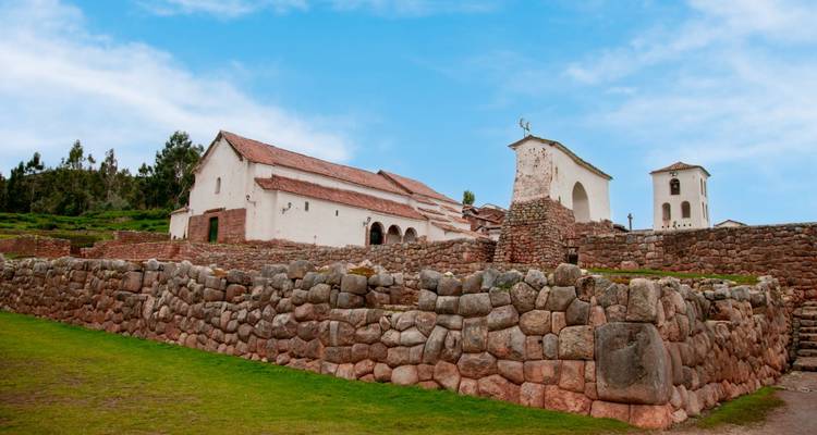 Église historique en adobe et clocher derrière des murs de pierre incas à Chinchero sous un ciel dégagé.