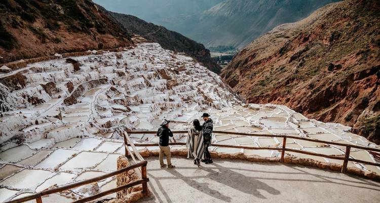 Des voyageurs en ponchos admirant les terrasses de sel géométriques de Maras qui cascadent le long d'un canyon.