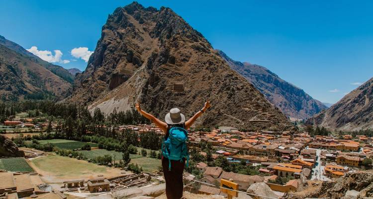 Voyageur avec sac à dos célébrant au sommet des ruines d'Ollantaytambo surplombant la ville et les montagnes spectaculaires.