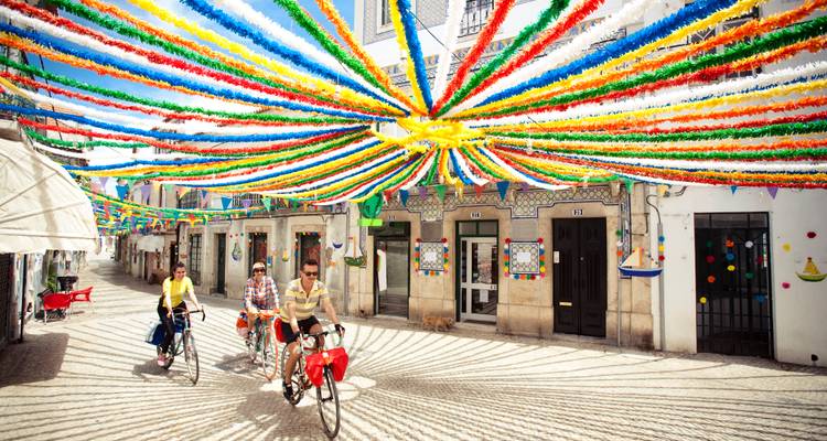 Fietsers rijden door een Portugese straat die versierd is met kleurrijke linten en helder zomerlicht.