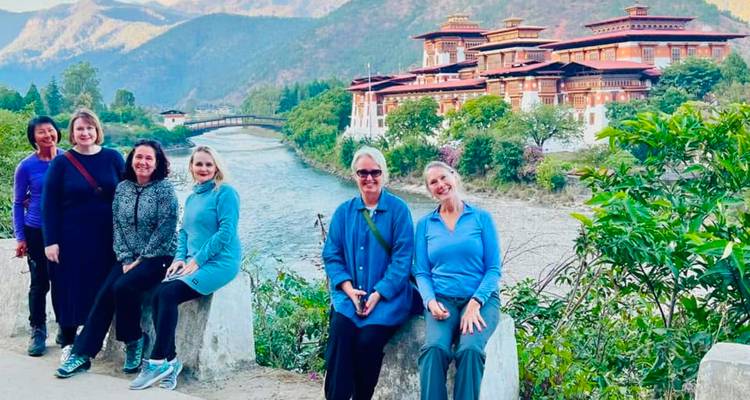 Groupe de voyageurs posant au bord d'une rivière avec le Punakha Dzong illuminé en arrière-plan.