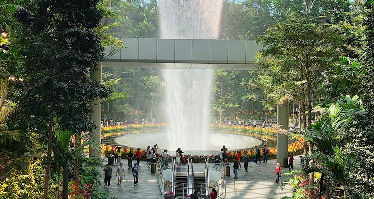 La cascade Rain Vortex dévale à travers les jardins forestiers intérieurs luxuriants de Jewel Changi Airport tandis que des foules de visiteurs observent.