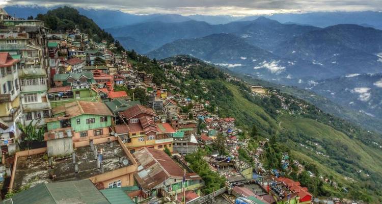 Panoramablick auf die Hangstadt Gangtok mit bunten Häusern, die sich über üppige Bergkämme hinab zu nebligen, geschichteten Bergen erstrecken.