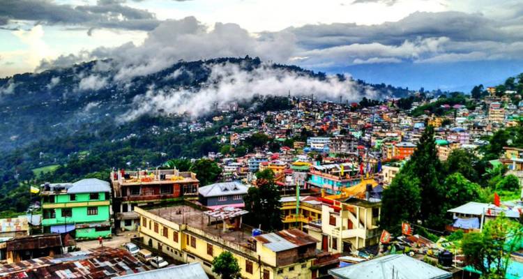 Farbig getünchte Häuser thronen auf einem nebligen Berghang unter dramatischer Wolkendecke in Kalimpong.