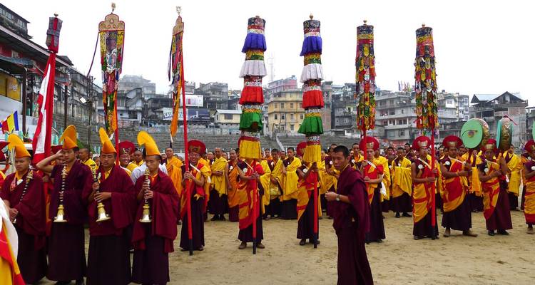 Große Versammlung buddhistischer Mönche in kastanienbraunen und gelben Gewändern, die hohe, verzierte Banner während eines Klosterfestes tragen.