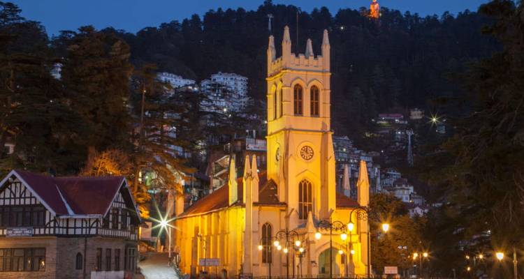 Erleuchtete neugotische Christuskirche vor dem bewaldeten Hang von Shimla in der Abenddämmerung.