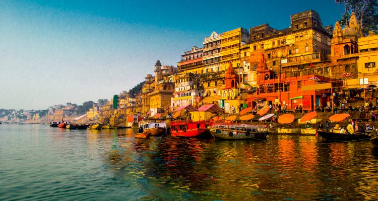 Les bâtiments aux couleurs vives et les temples du bord de la rivière à Varanasi se reflètent dans le Gange sous un ciel matinal dégagé.