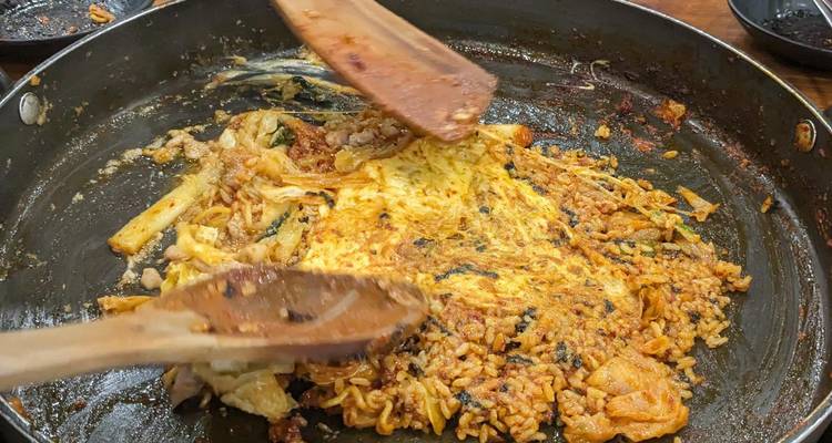 Una sartén chisporroteante de arroz frito coreano y verduras se revuelve con espátulas de madera durante la cocción.