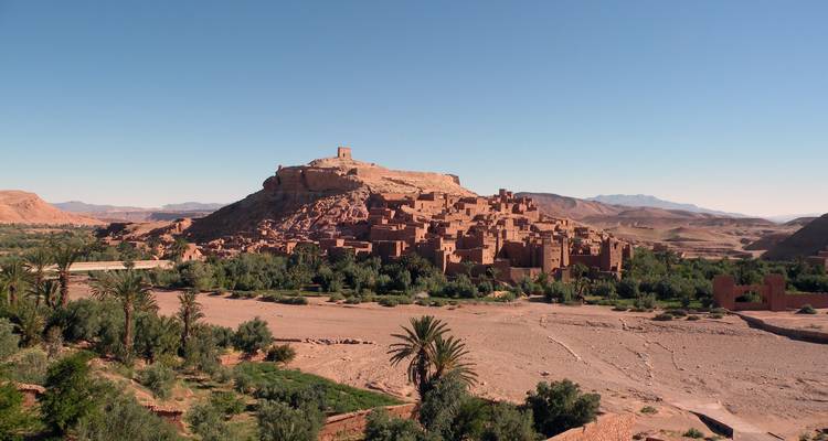 Panoramablick auf die aus Lehm erbaute Kasbah von Aït Benhaddou, die sich über einem ausgetrockneten Flussbett erhebt.