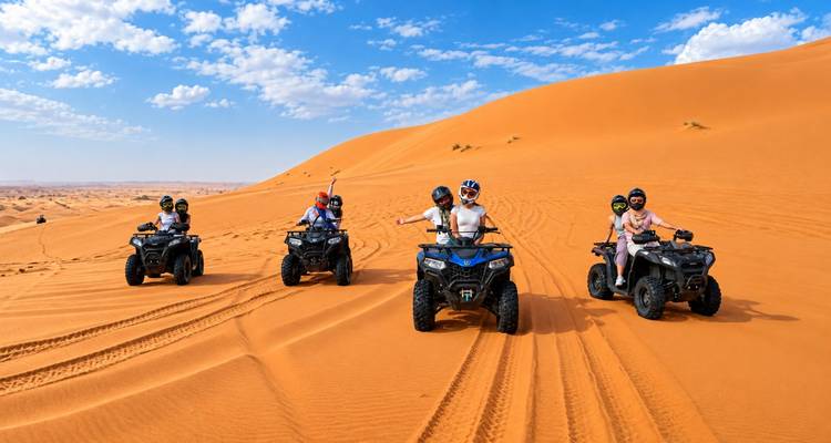 Cinco jinetes aceleran a través de enormes dunas naranjas en quads, dejando pistas barredoras bajo un cielo azul brillante.