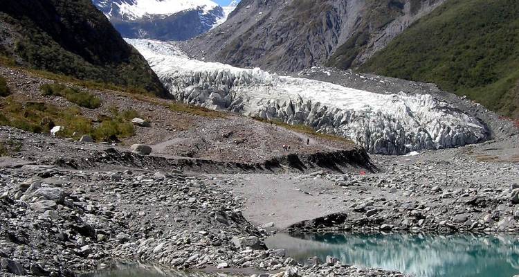 Terminus d'un glacier avec de la glace déchiquetée et un petit bassin d'eau de fonte turquoise dans la vallée.
