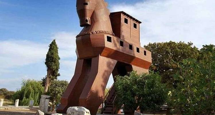 Large wooden replica of the Trojan Horse stands among trees under blue sky.