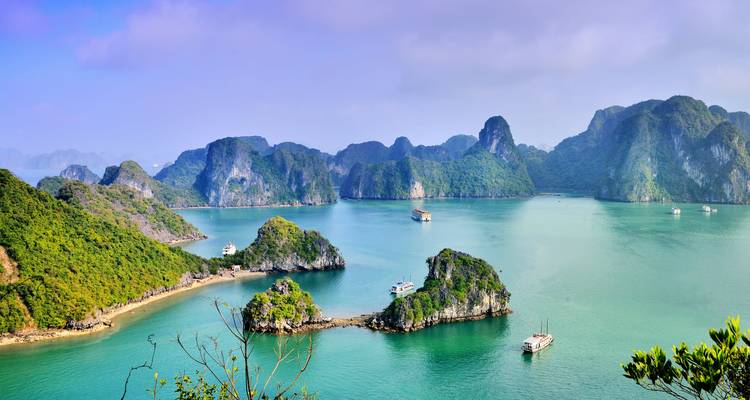 Vista panorámica de islotes esmeralda y agua turquesa de la Bahía de Ha Long salpicada de barcos de crucero bajo un cielo brumoso