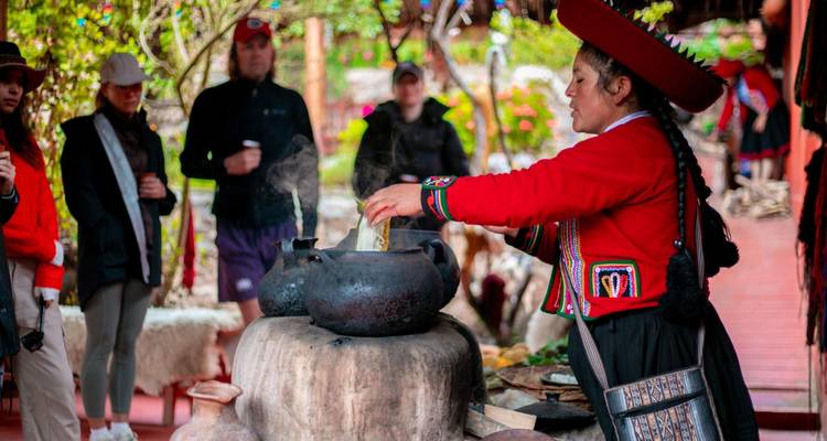Femme andine en tenue rouge traditionnelle prépare de la nourriture au-dessus de pots en argile fumants tandis que des voyageurs observent à l'intérieur d'un atelier rustique.