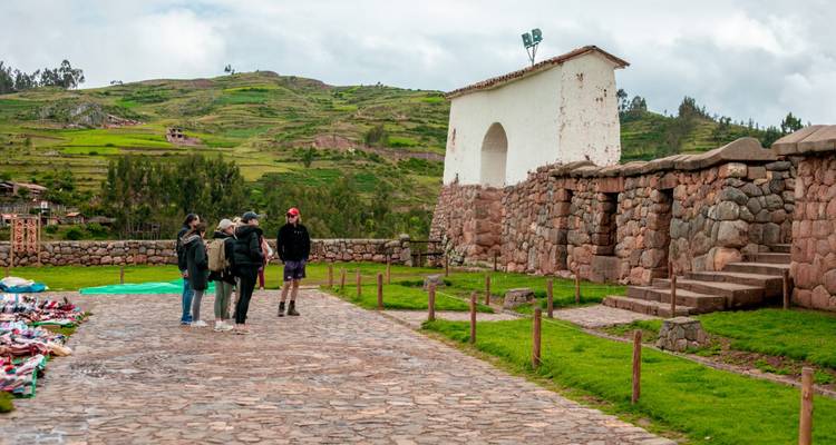 Petit groupe de touristes écoutant un guide devant des murs de pierre et une arche au milieu des collines vertes dans les Andes.