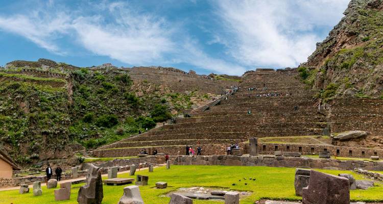 Scène panoramique des ruines incas d'Ollantaytambo avec des terrasses de pierre s'élevant sur une falaise escarpée sous un ciel bleu éclatant.